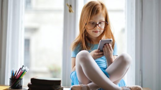 young-red-haired-child-sitting-don-by-window-using-phone